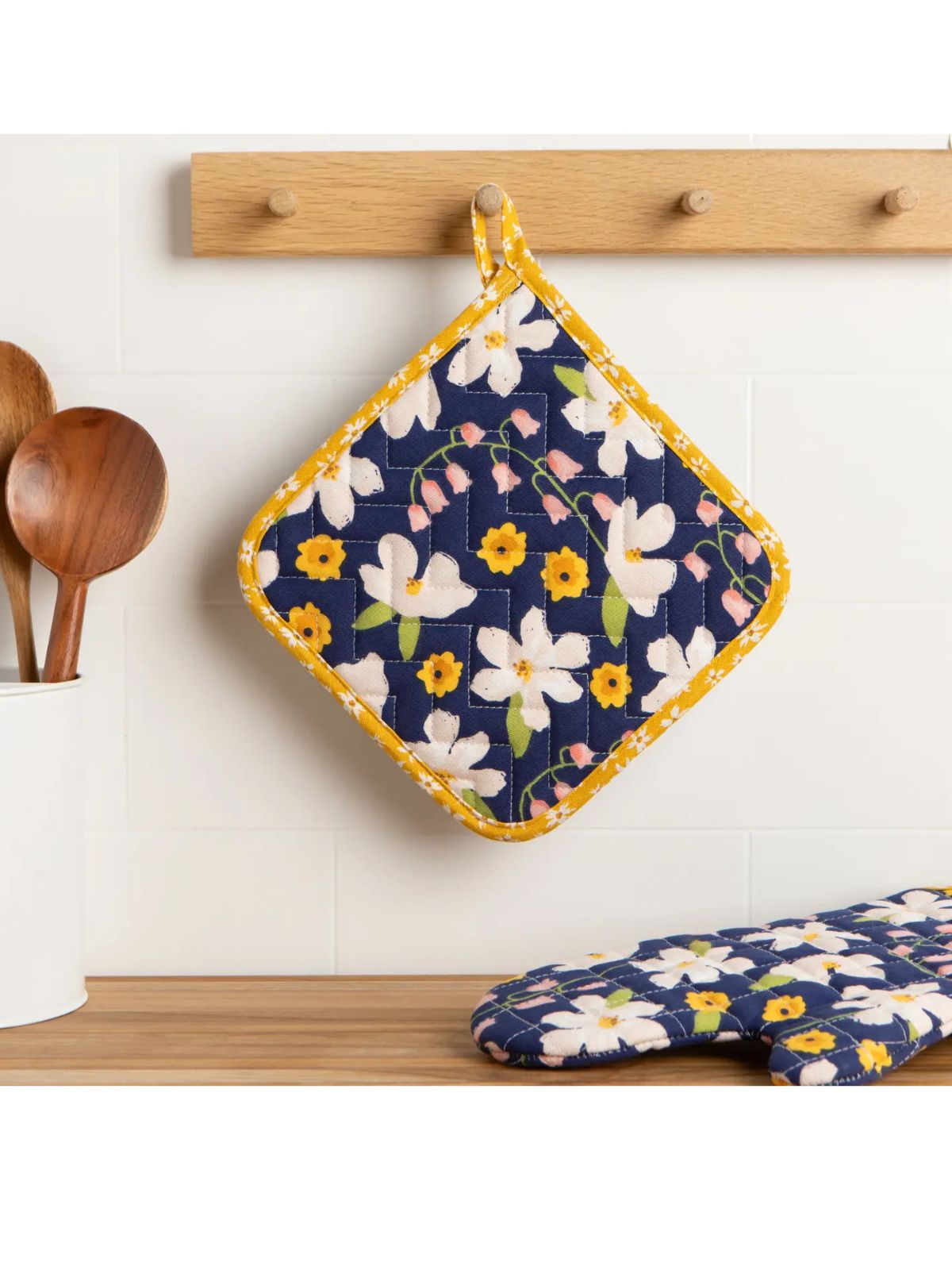 Floral patterned pot holder and oven mitt hanging on a wooden rack.