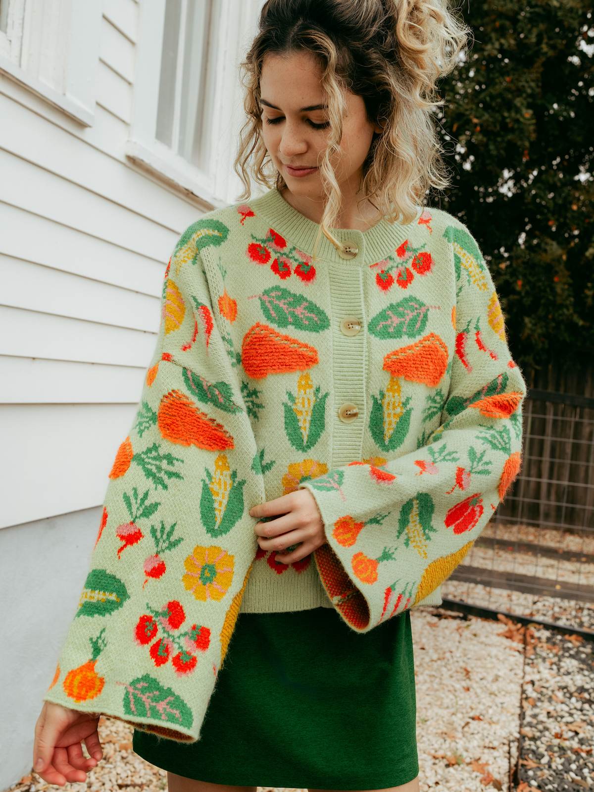 Woman wearing a colorful knitted cardigan with vegetable patterns outdoors.