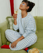 Woman in checkered pajamas holding a glass of champagne on a green couch.