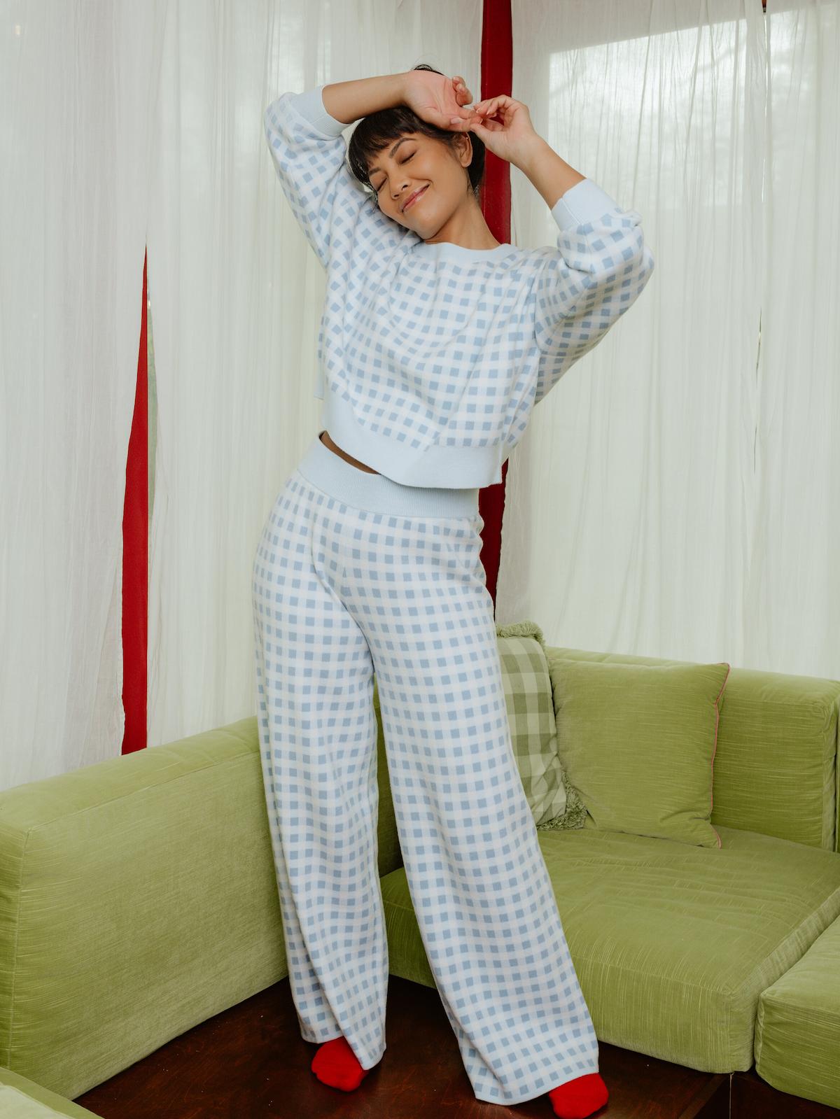 Person wearing a checkered outfit standing in a room with green furniture and white curtains.