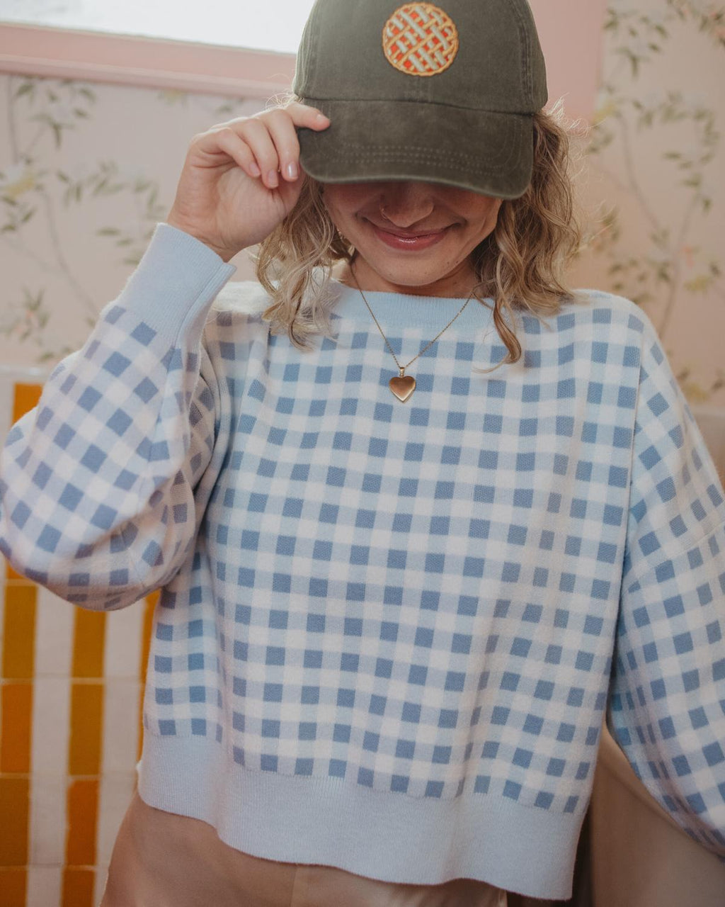 Person wearing a green cap with a logo and a blue checkered shirt.