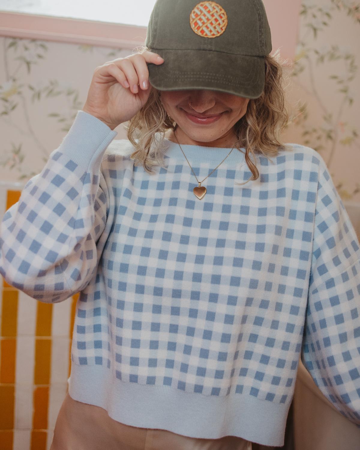 Person wearing a green cap with a logo and a blue checkered shirt.