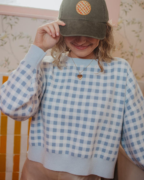 Person wearing a green cap with a logo and a blue checkered shirt.