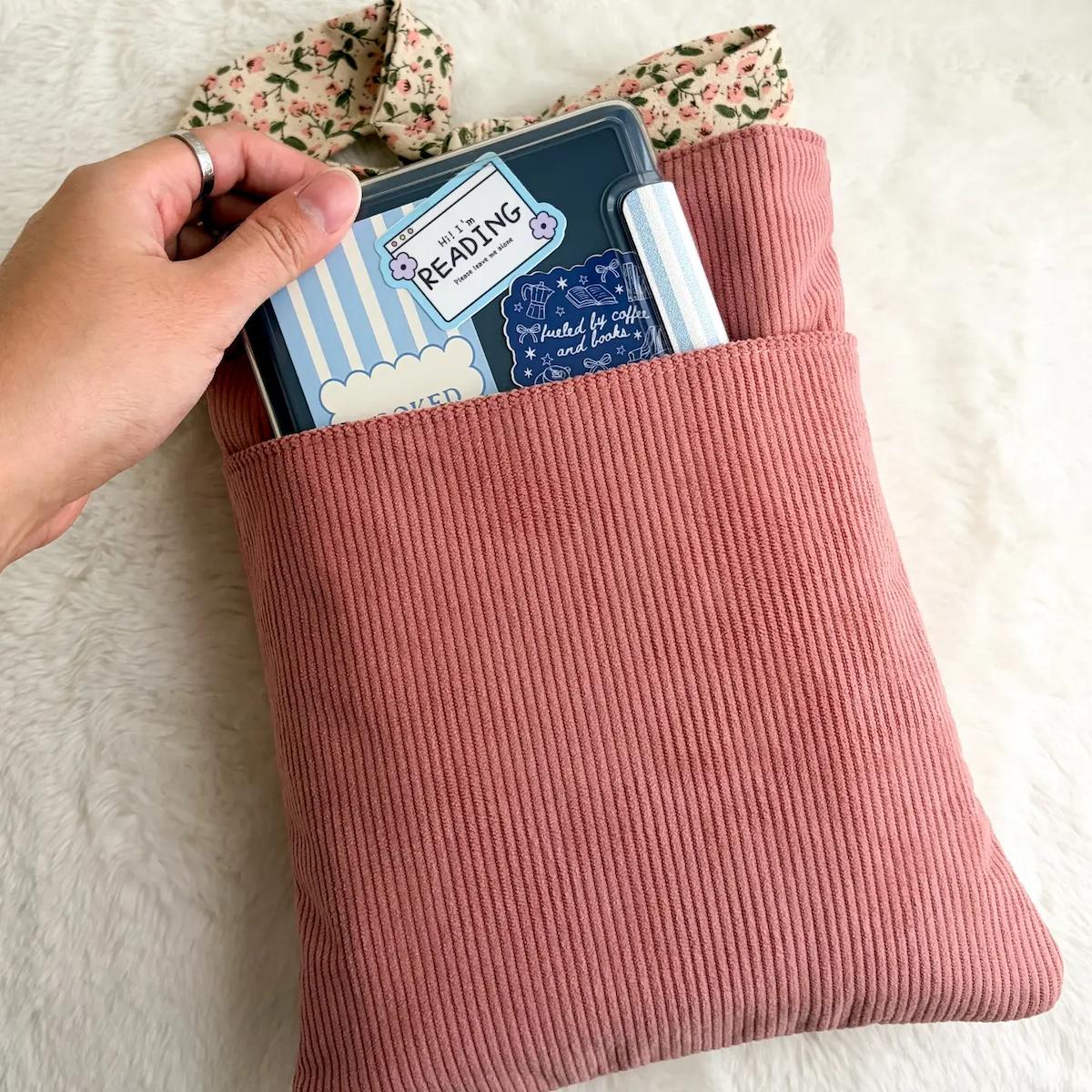 Pink textured pouch with books inside, held by a hand on a light background