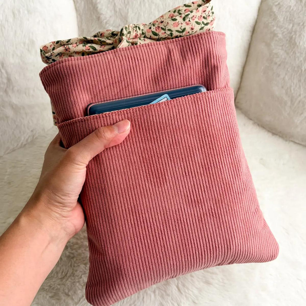 Pink corduroy bag with a floral item peeking out, held by a hand against a neutral background.