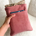 Pink corduroy bag with a floral item peeking out, held by a hand against a neutral background.