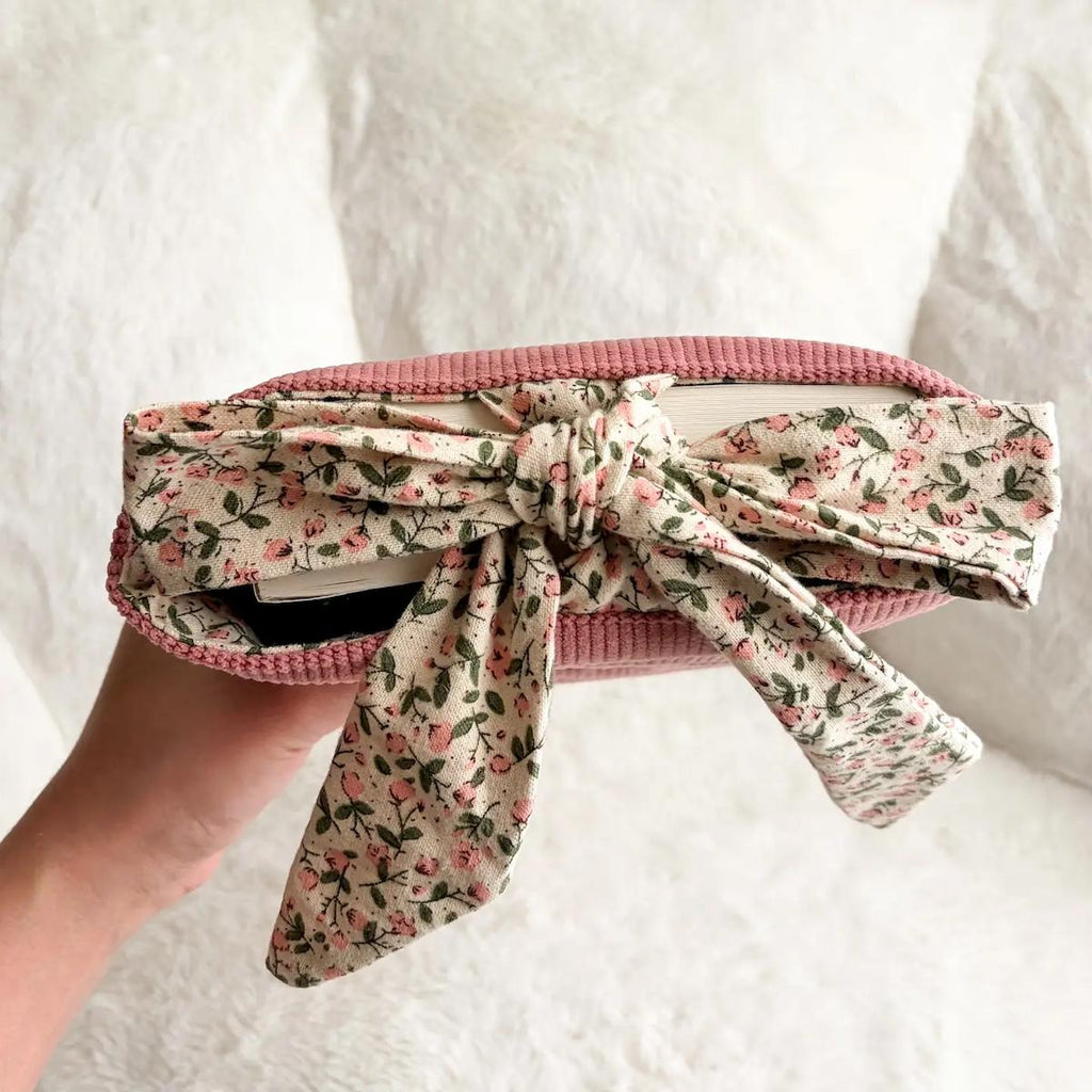 Floral-patterned belt with a pink trim held by a person on a white background