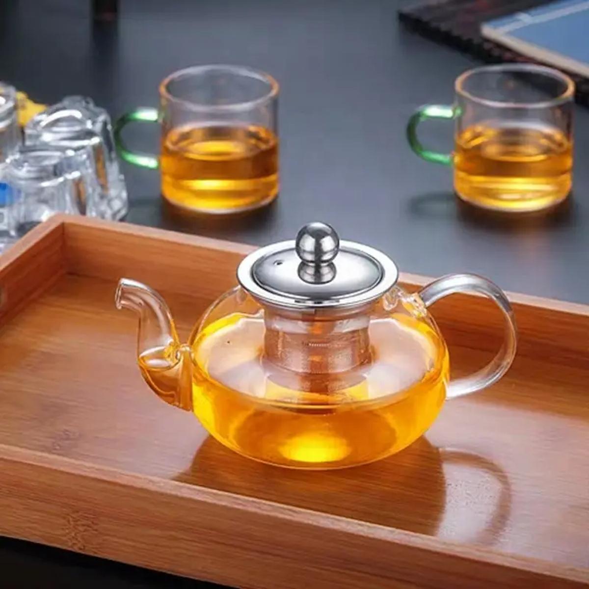 Glass teapot with a silver lid on a wooden tray, surrounded by glass cups with tea.