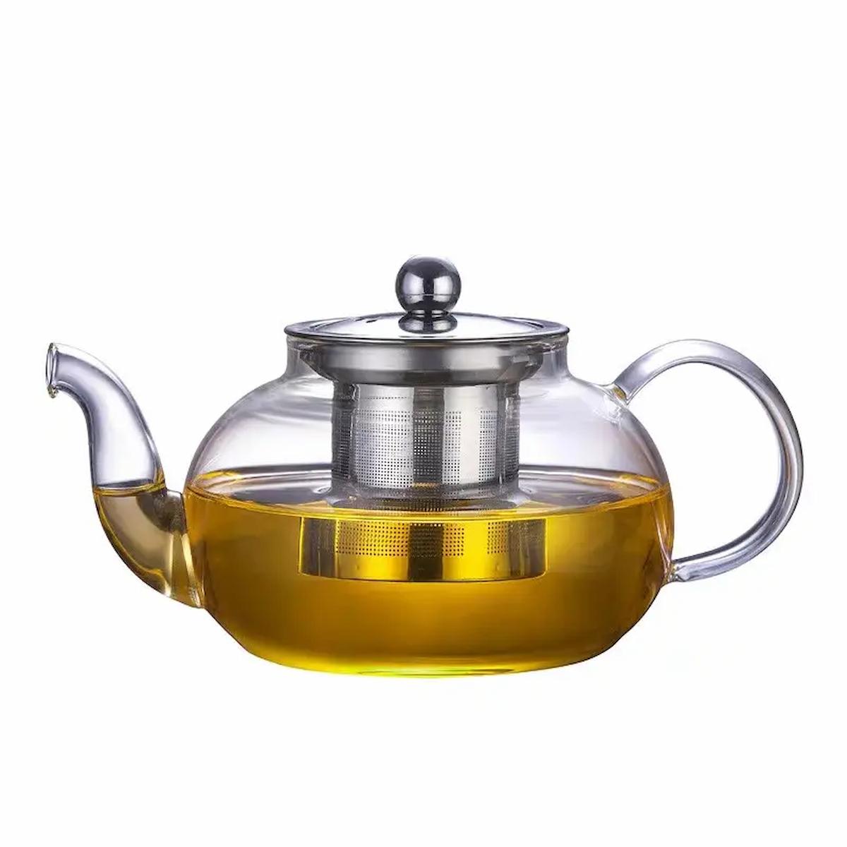 Clear glass teapot with metal lid and handle filled with yellow liquid on a white background