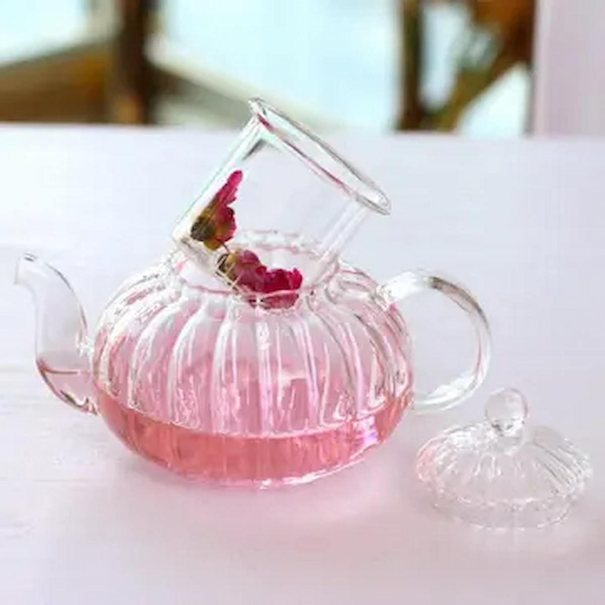 Glass teapot with pink liquid and flowers on a white surface