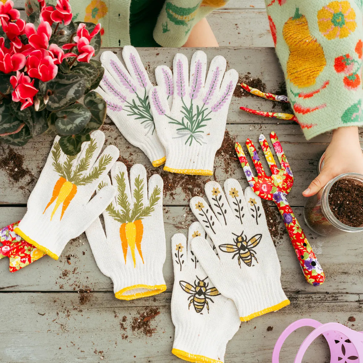 Gardening gloves with plant designs on a wooden surface with gardening tools and plants.