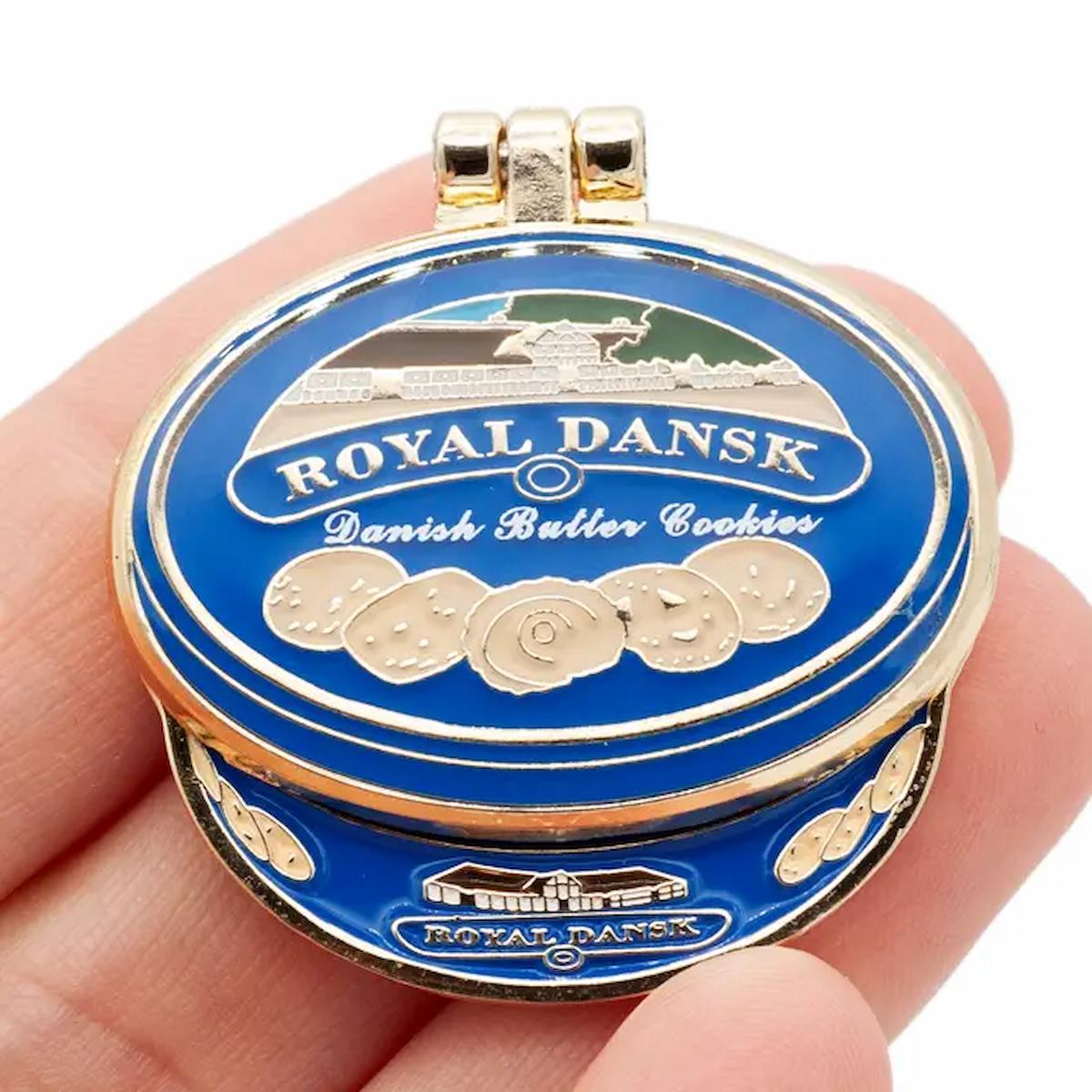 Blue cookie tin with gold accents and 'Royal Dansk' branding held in a hand.