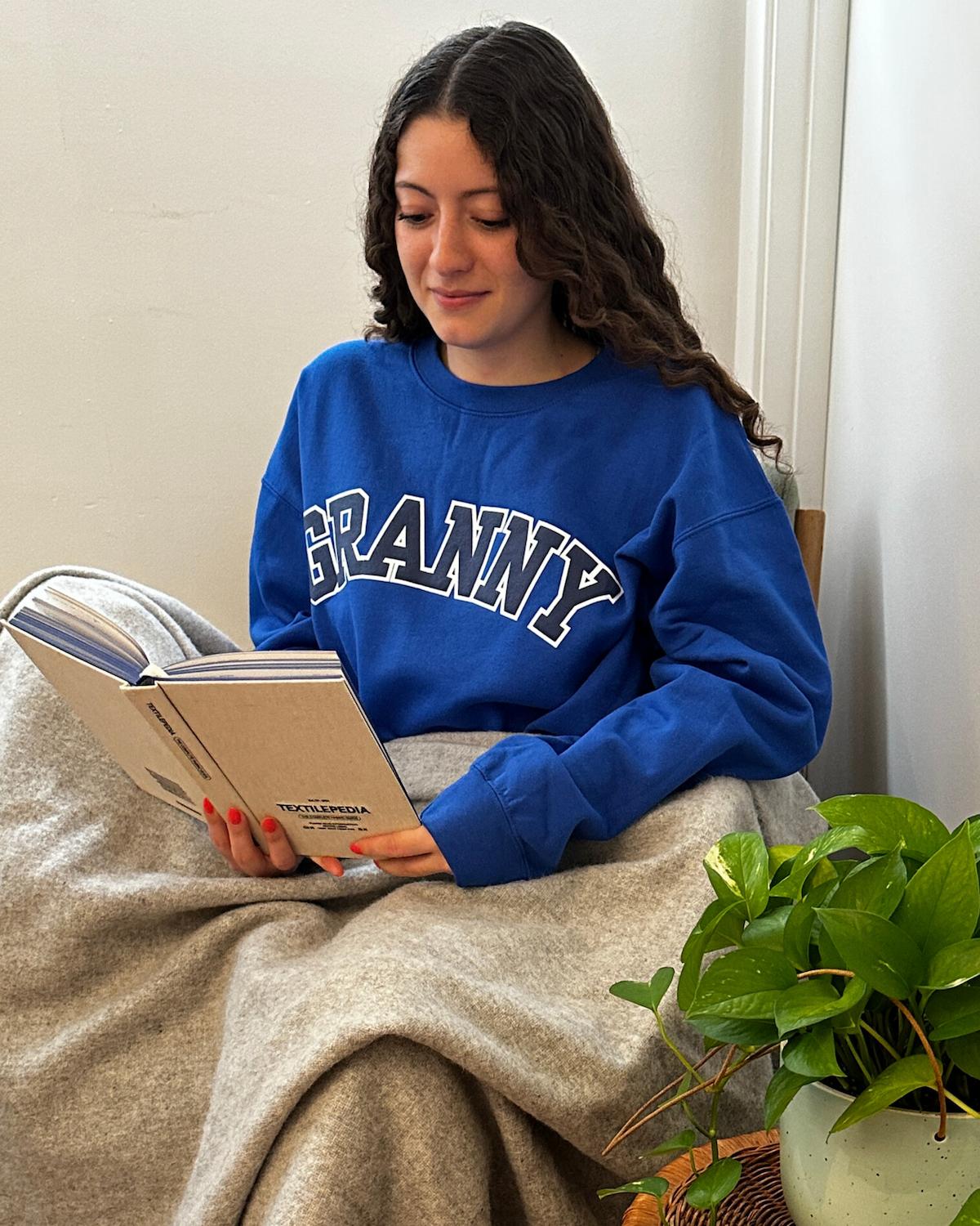 Person wearing a blue sweatshirt with 'GRANNY' printed on it, reading a book indoors.