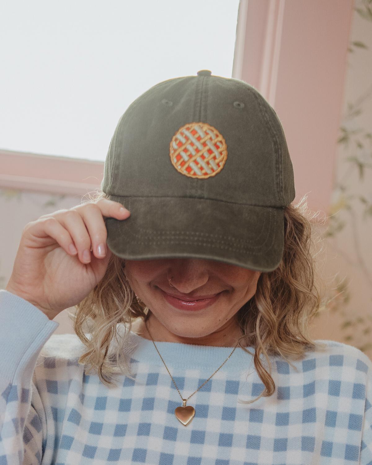 Person wearing a green cap with a circular logo, smiling indoors.