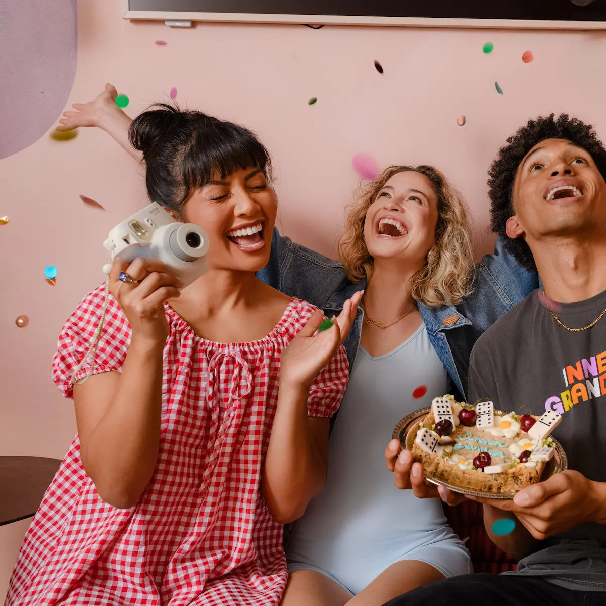 Three friends celebrating with a cake and confetti in a room.