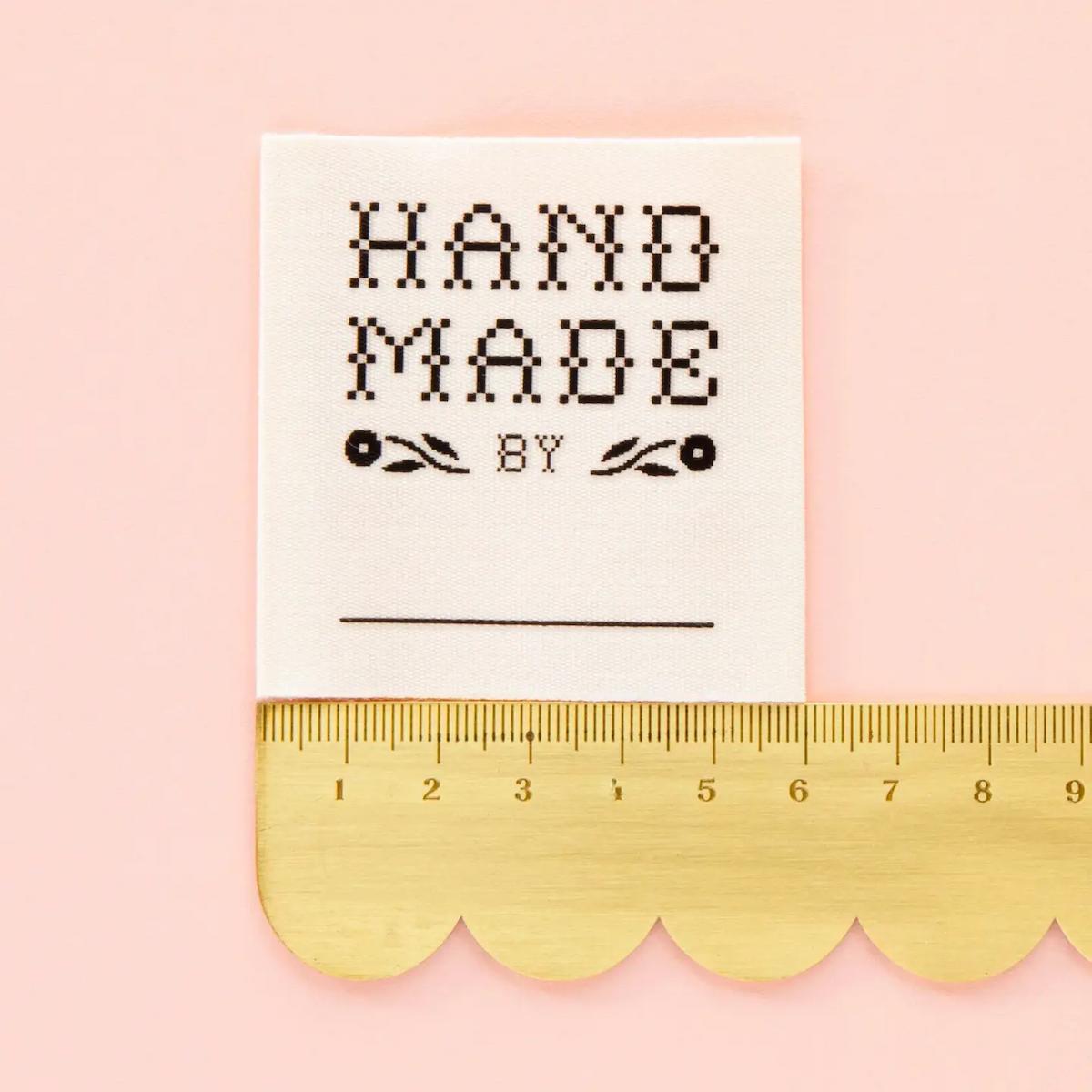 Label with 'Hand Made by' text on a pink background with a gold ruler at the bottom.