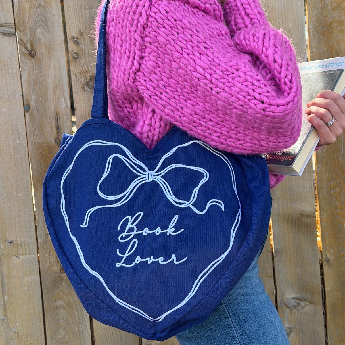 Person holding a blue bag with 'Book Lover' design against a wooden background