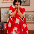 Woman wrapped in a red and white patterned shawl in a room with framed pictures on the wall.
