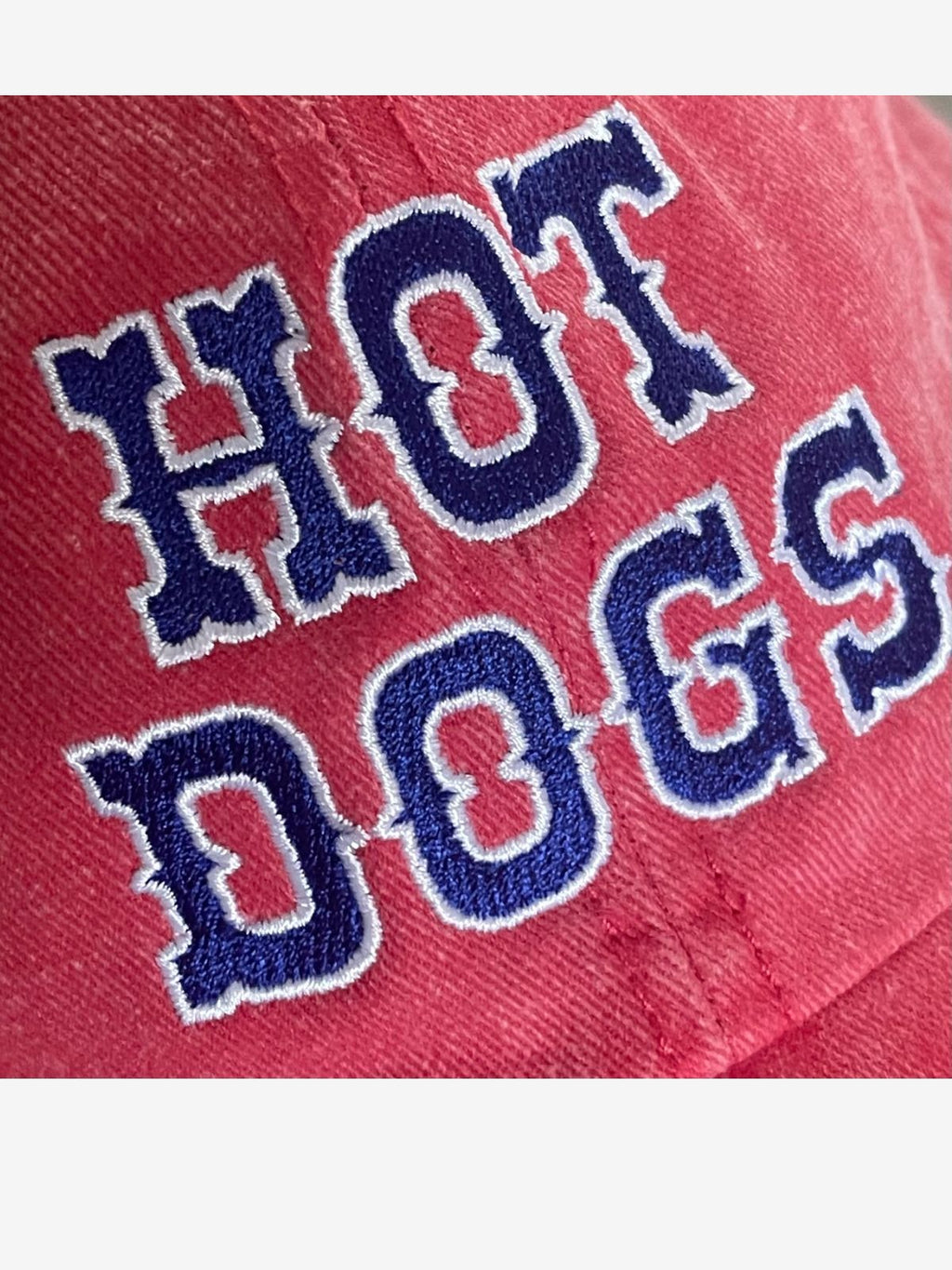 Close up of red baseball cap with 'Hot Dogs' embroidered in blue and white 