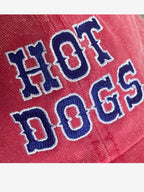 Close up of red baseball cap with 'Hot Dogs' embroidered in blue and white 