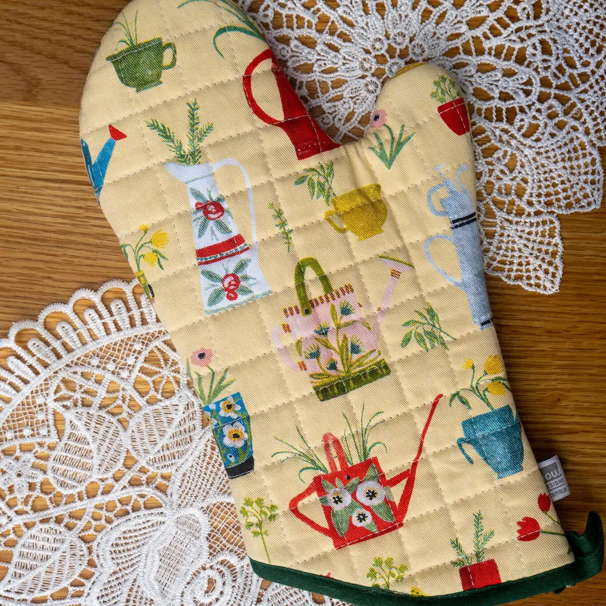 Pair of oven mitts with gardening-themed design on a lace doily.