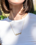 Person wearing a gold necklace with 'Sasha' on a white shirt outdoors