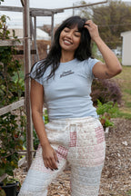 Woman wearing a light blue t-shirt and patterned pants standing in an outdoor garden setting.