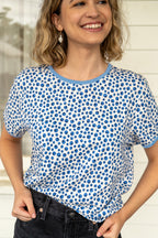 Model wearing a blueberry print tee with a light blue collar in front of a white house