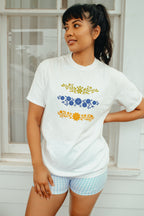 Woman wearing a white t-shirt with Pyrex designs in blue and yellow, standing in front of a white window.