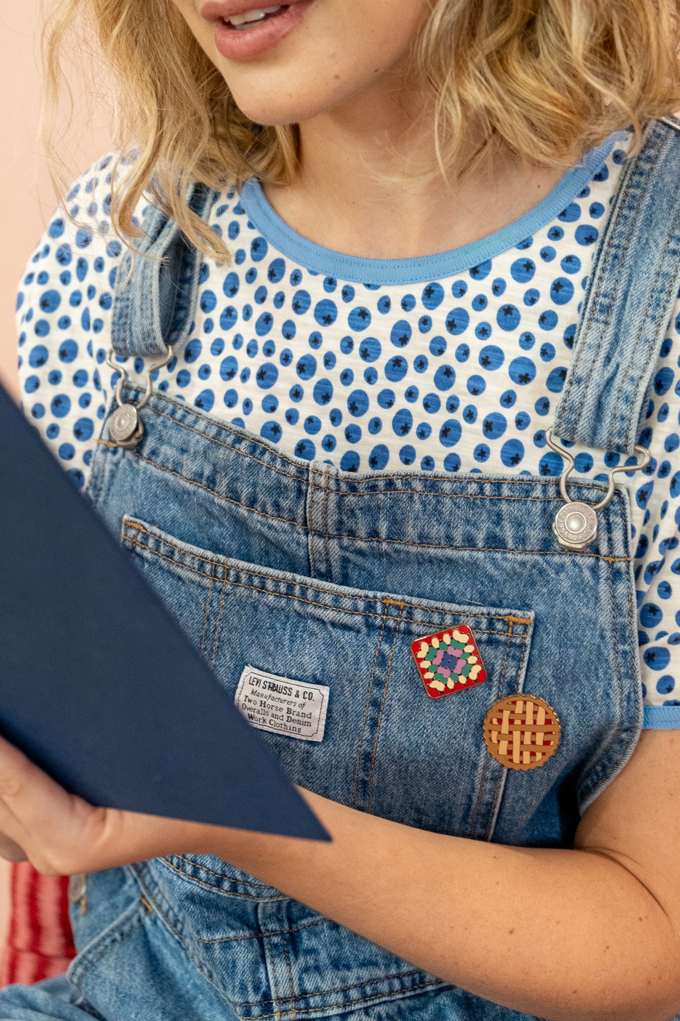 close up of the blueberry print under overalls while the model reads