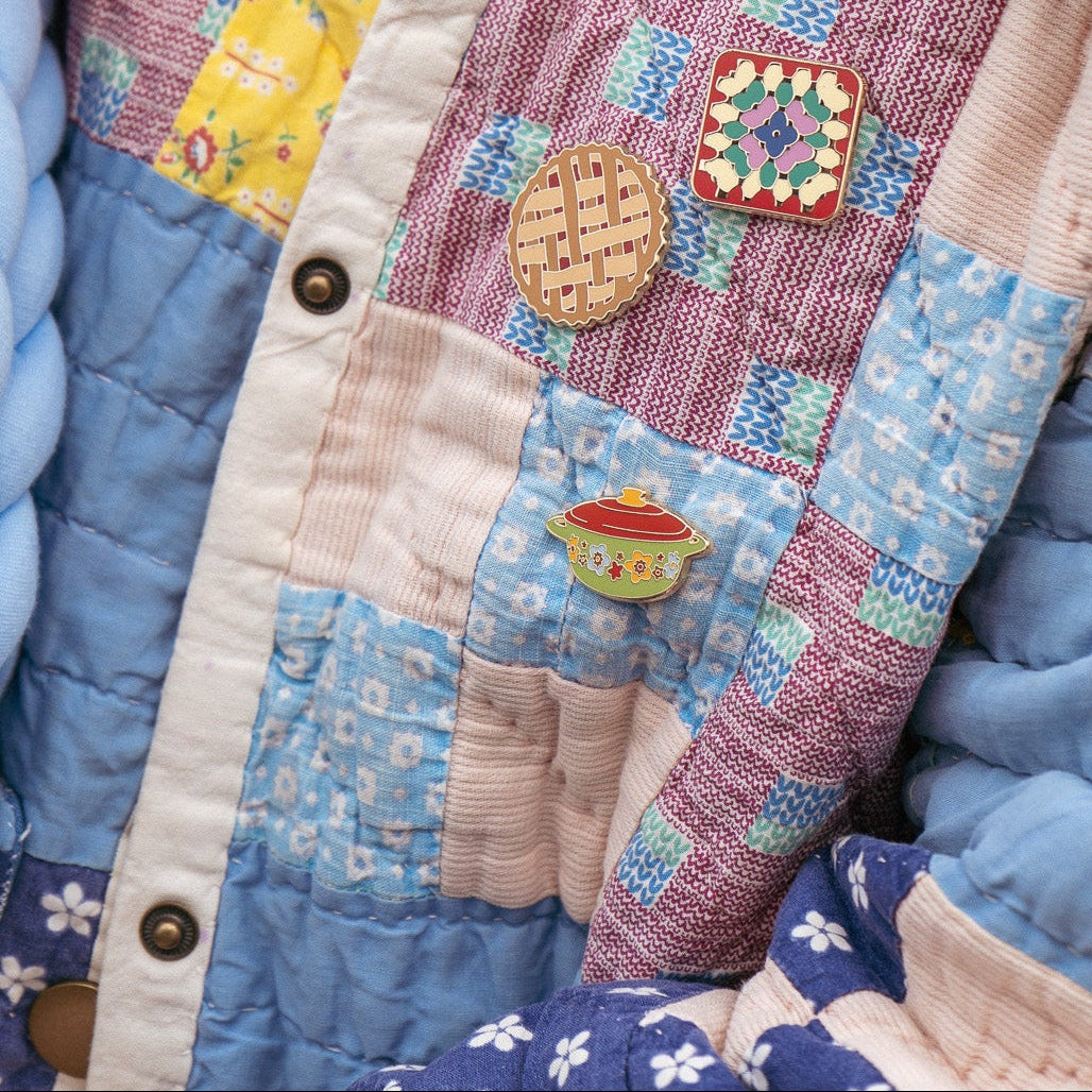 Woman wearing a denim jacket with hot dish pin and grandma quilt pin against a hoodie background
