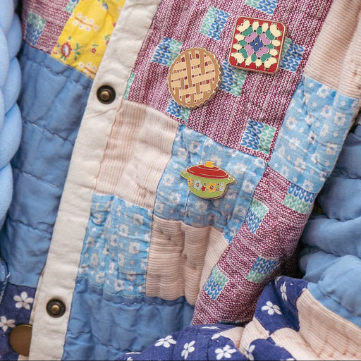 Woman wearing a denim jacket with hot dish pin and grandma quilt pin against a hoodie background