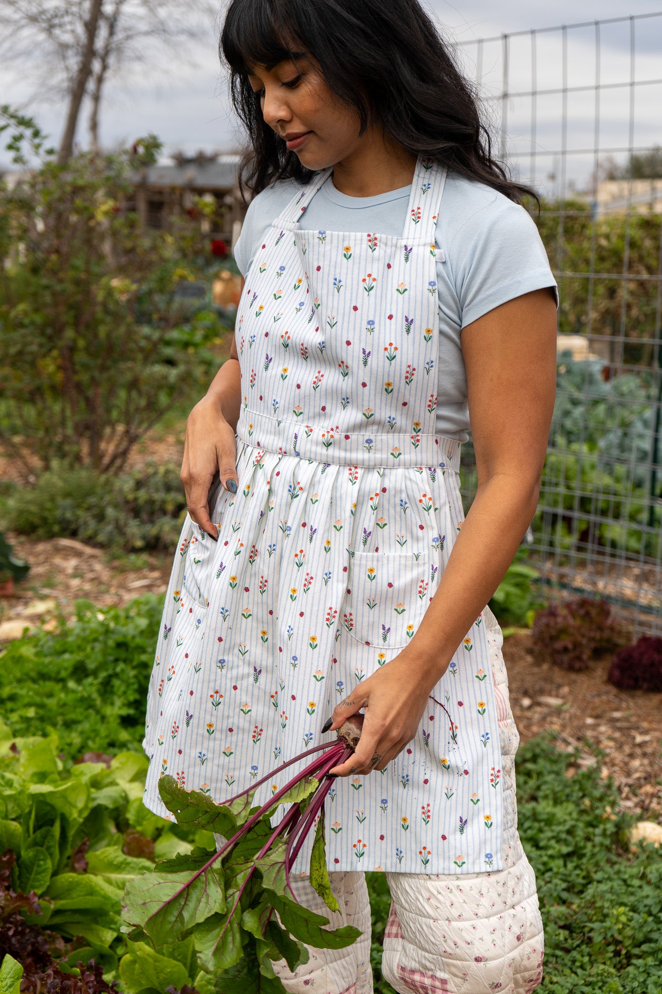Women in garden with floral print apron with veggies in hand