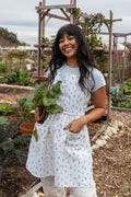 Woman wearing a floral tie back apron in garden with veggies in front pocket of apron