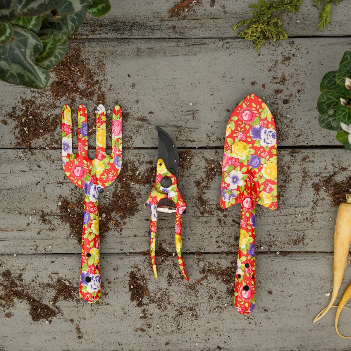 Colorful garden tools on a wooden surface with plants and carrots. 