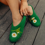 Green slippers with floral designs worn on a wooden floor