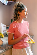 Woman in a kitchen wearing a red gingham tee holding a teacup. 