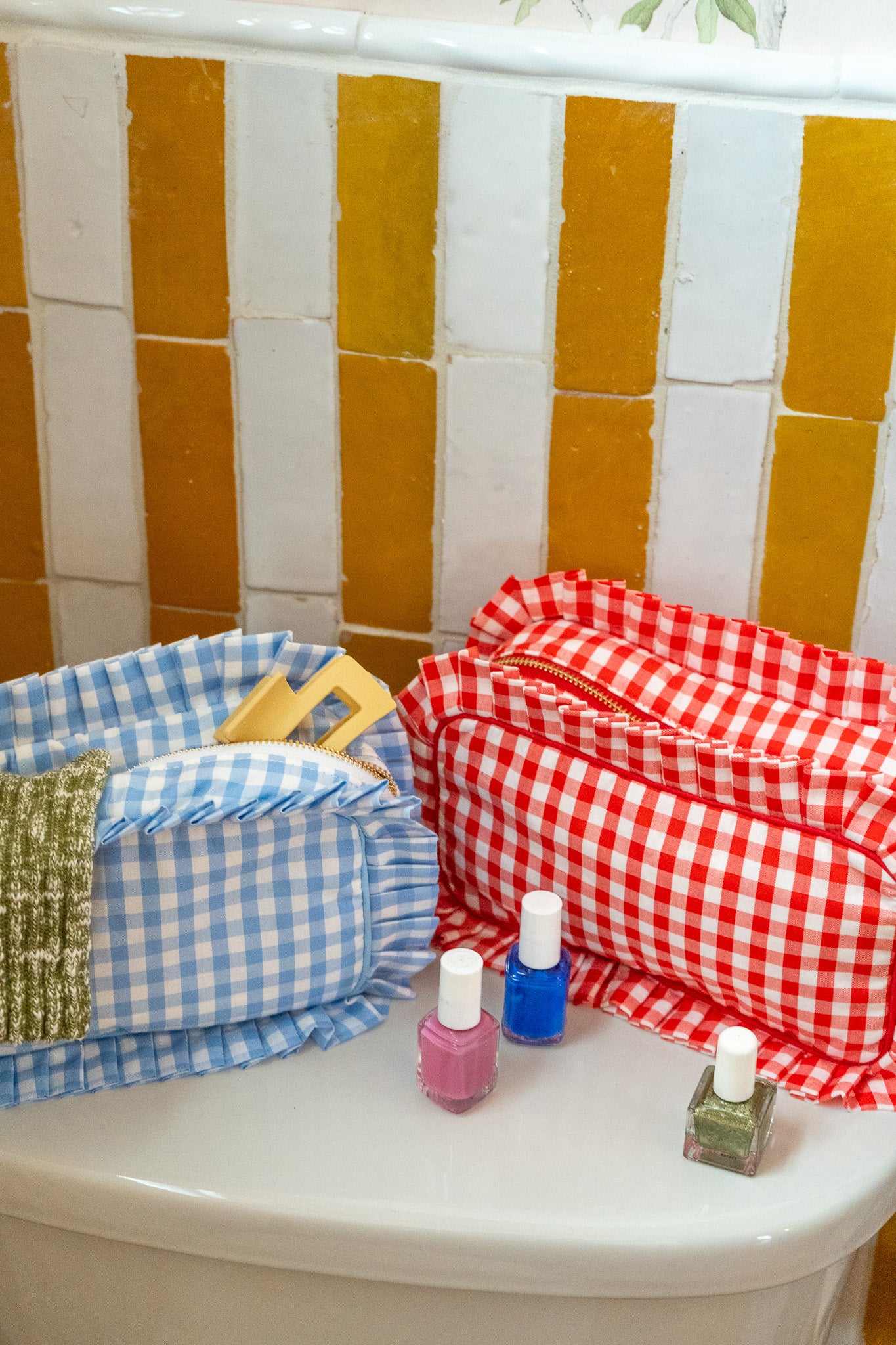 Nail polish bottles on a white surface with a checkered basket and red gingham towel in the background.