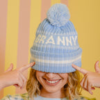 Person wearing a blue 'GRANNY' beanie with a pom-pom against a striped background