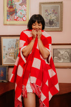 Woman wrapped in a red and white patterned shawl in a room with framed pictures on the wall.