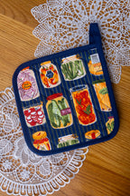Potholder with jarred vegetables design on a wood table with doily