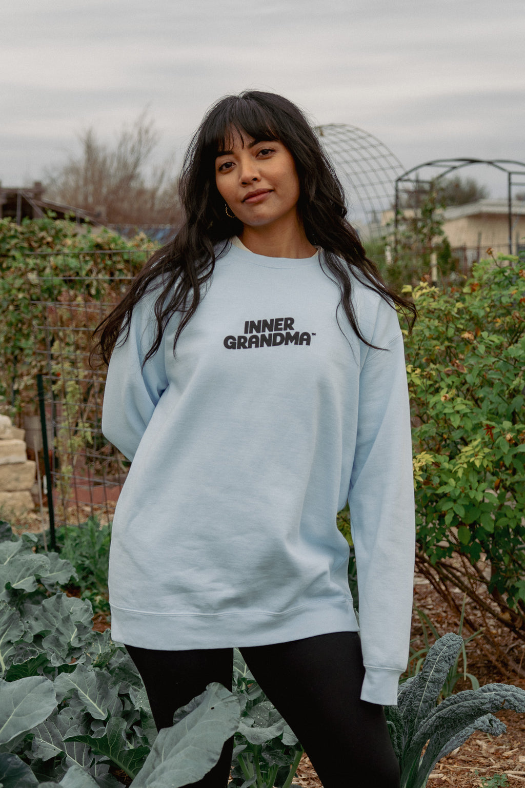 Front view of light blue sweatshirt that says inner grandma with a garden background