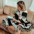 Woman sitting on a couch with a cozy shawl, reading a book in a cozy living room.