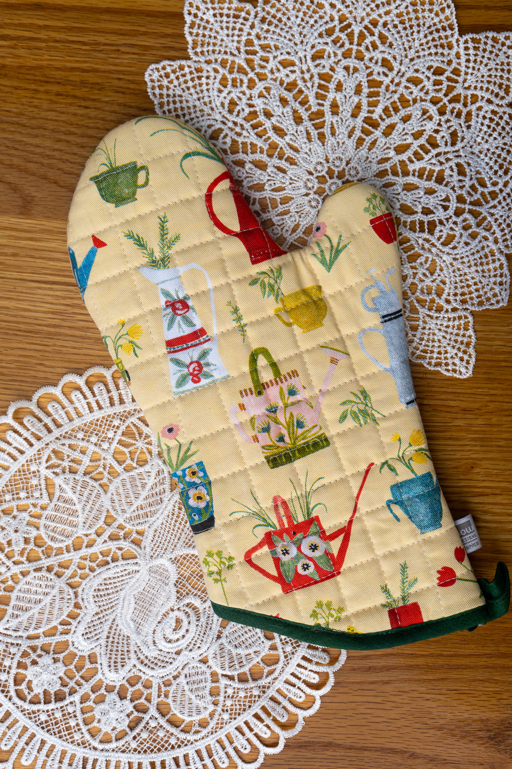 Oven mitt with gardening-themed pattern on a wood table with doilys 