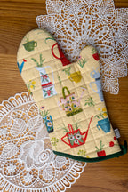 Oven mitt with gardening-themed pattern on a wood table with doilys 