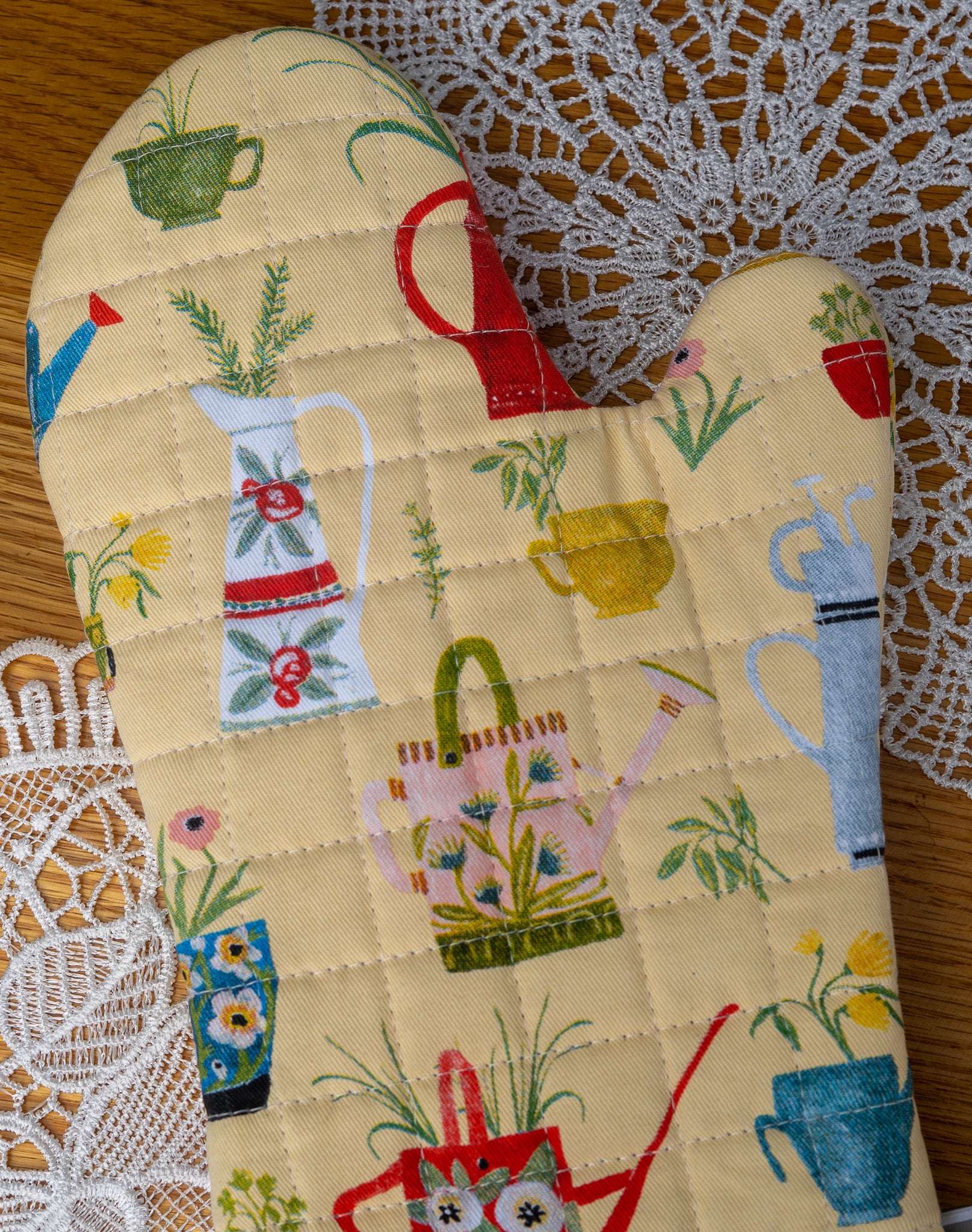 Close up of watering can print on oven mitt that sits on a wood table