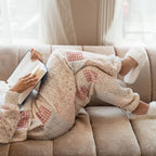 Person sitting on a couch with a blanket and book, surrounded by soft light