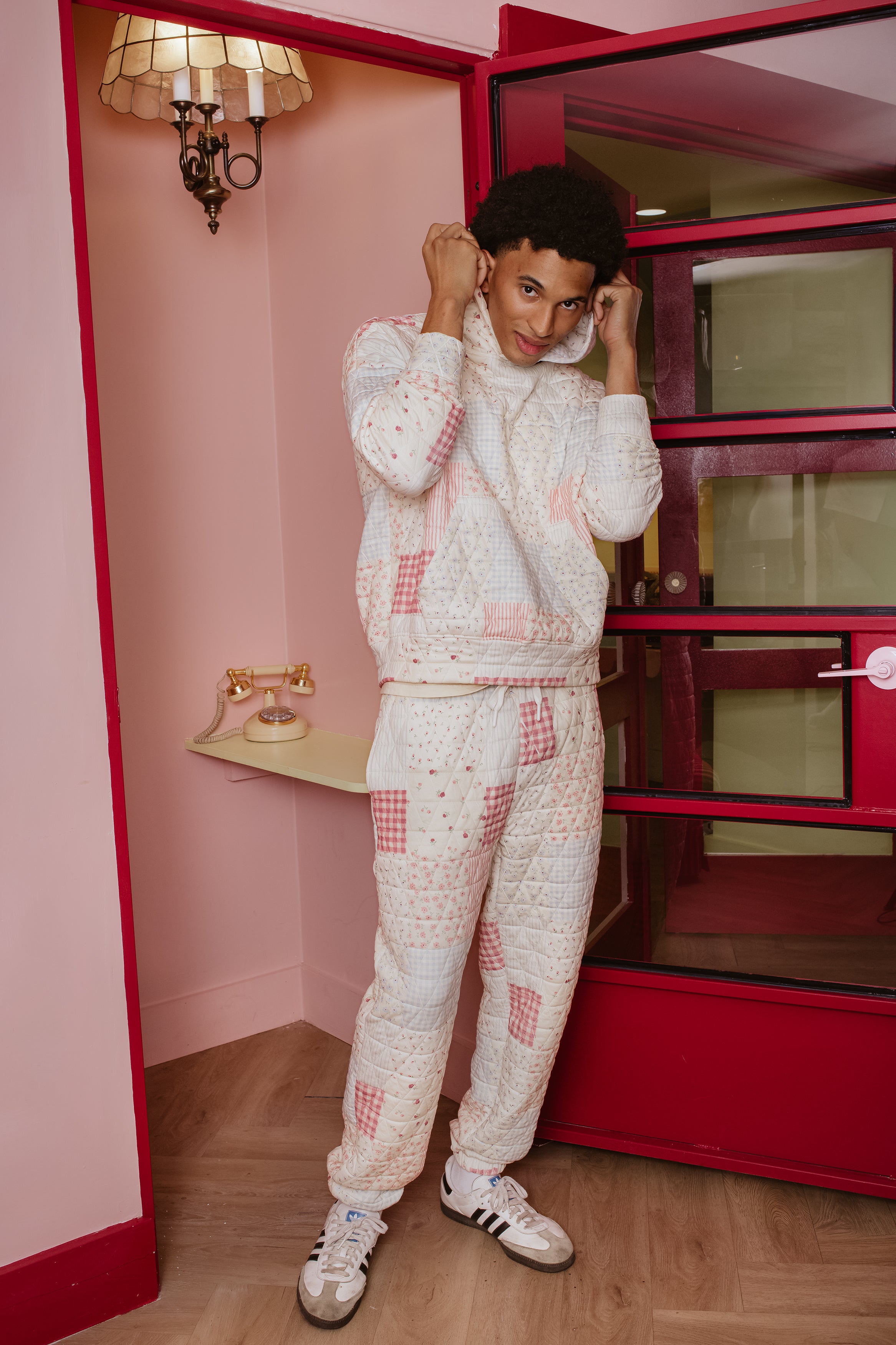 Person wearing a matching patchwork outfit in a room with pink walls and a red wardrobe.