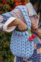 Light blue large knot bag on shoulder of women with crochet red flowers on strap. 