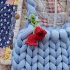 Blue braided fabric with a red knitted flower on a quilted background